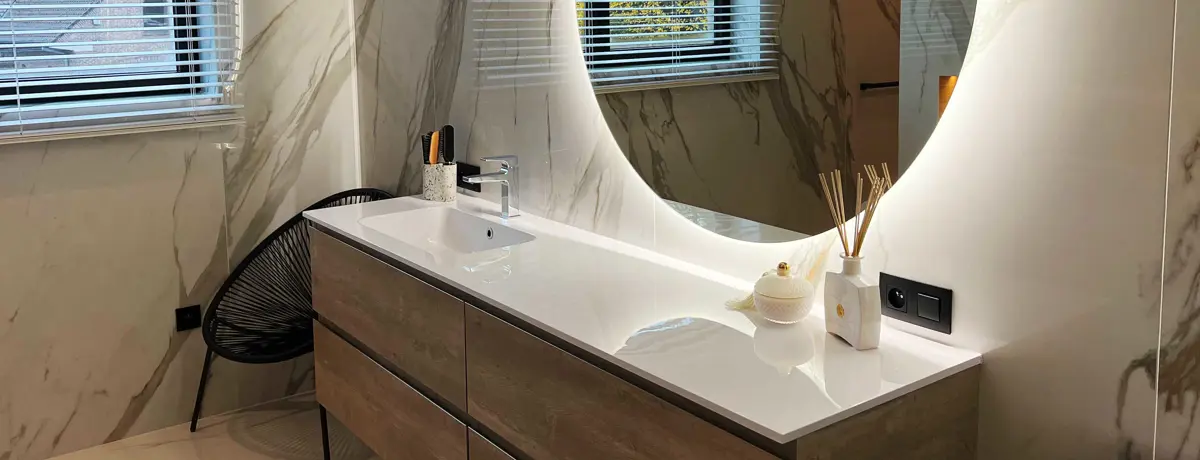 Badkamermeubel met wastafel en ronde spiegel tegen een wand met marmerlook. Meuble de salle de bains avec lavabo et miroir rond contre un mur à l’aspect marbré