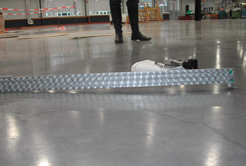 Mesure de la planéité d’un plancher sous une latte rigide de 2 m. La planéité relevée est hors tolérance puisque l’extrémité de la latte ne touche plus le sol.